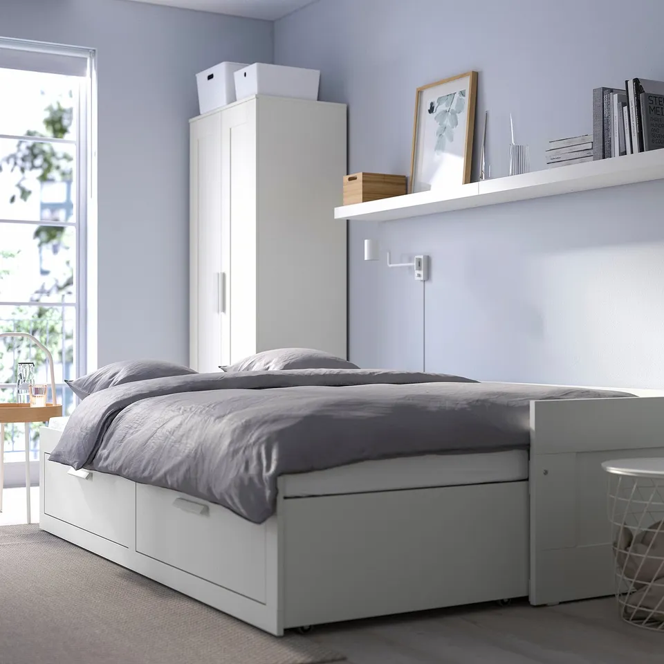 Modern bedroom with white BRIMNES day-bed, grey bedding, natalia chair, and floating shelf with decor. Tall vertical storage unit behind bed.