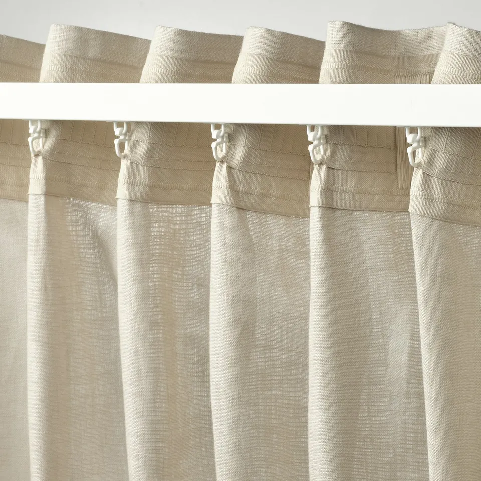 Beige linen curtains with pleats pinned by silver hooks on metal rod.