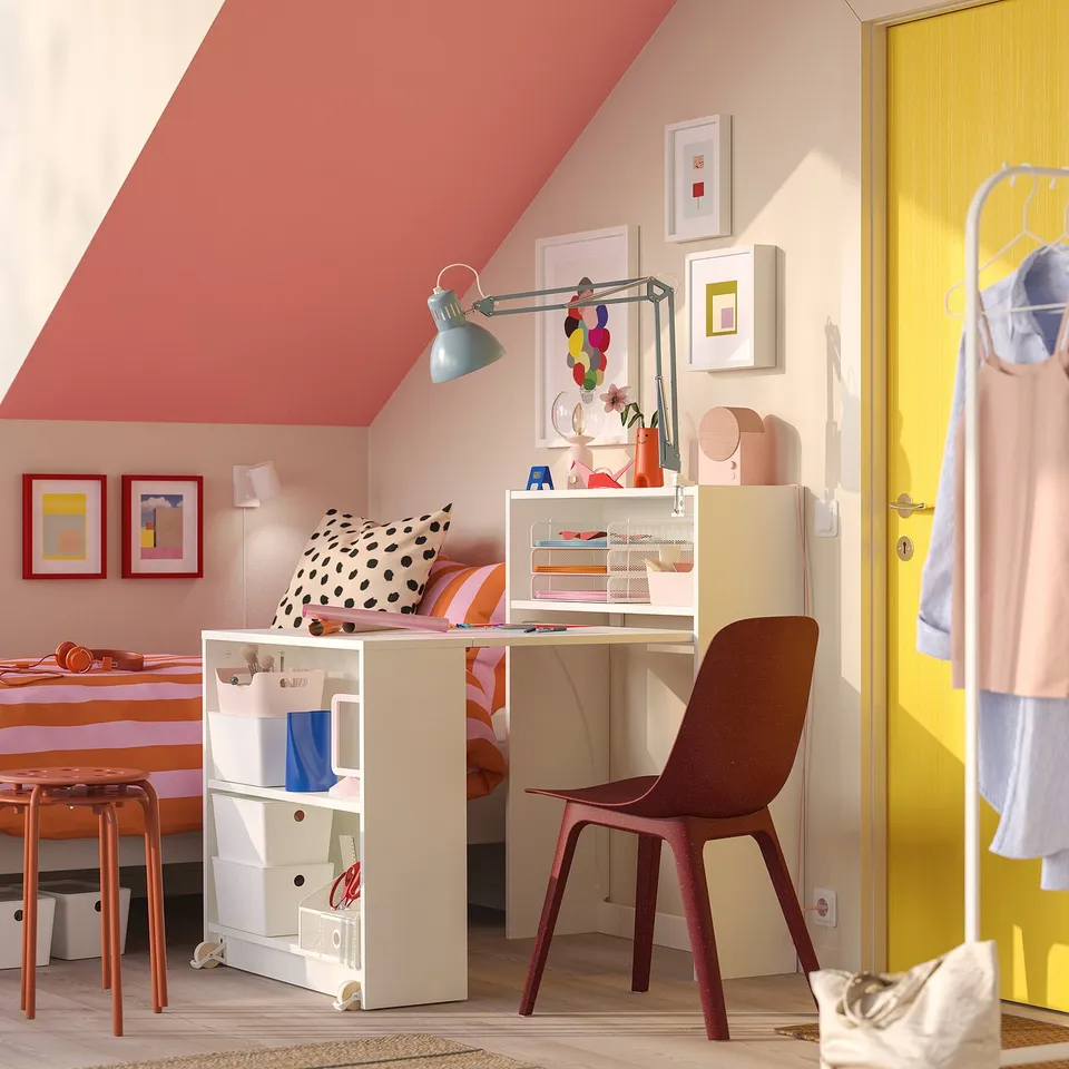 Bright attic office with BILLY bookcase-desk combo. White BILLY, red chair, colourful art, yellow door. Optimal use of small space.