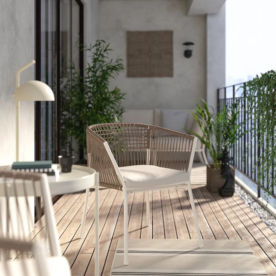 Balcony with white SEGERÖN wicker chair, cushion, lamp, and plants. Modern, minimalist design.