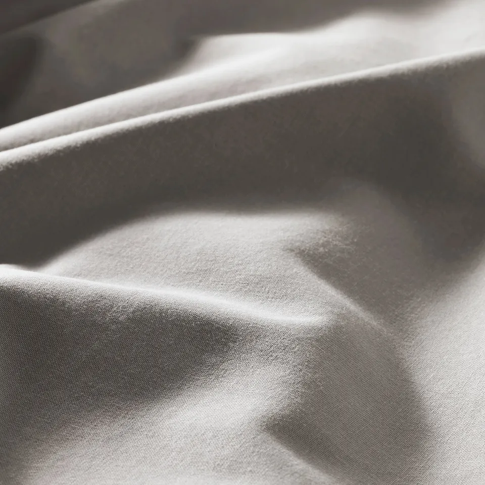 Close-up of soft, textured duvet cover in neutral shade. Light plays on smooth, wrinkled fabric, highlighting its quality and softness.