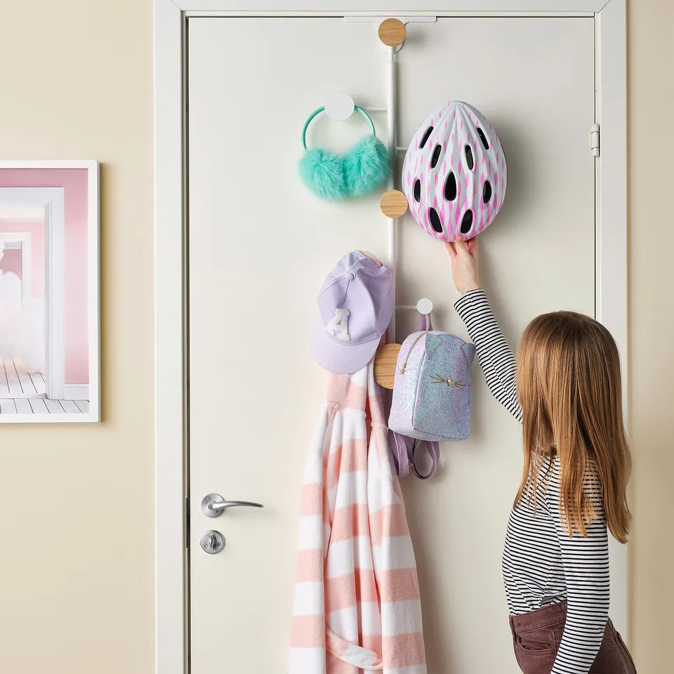 A child reaches for a helmet on a vertical door hanger, showing its use for storing accessories and clothes.
