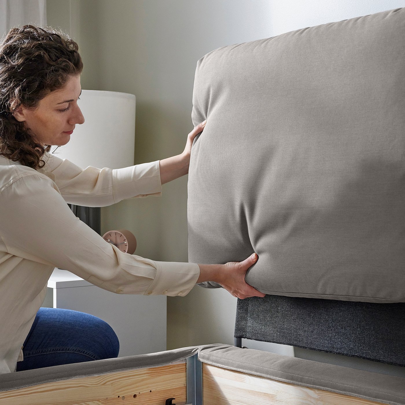 Person adjusting soft, sloped bed frame with pillows.