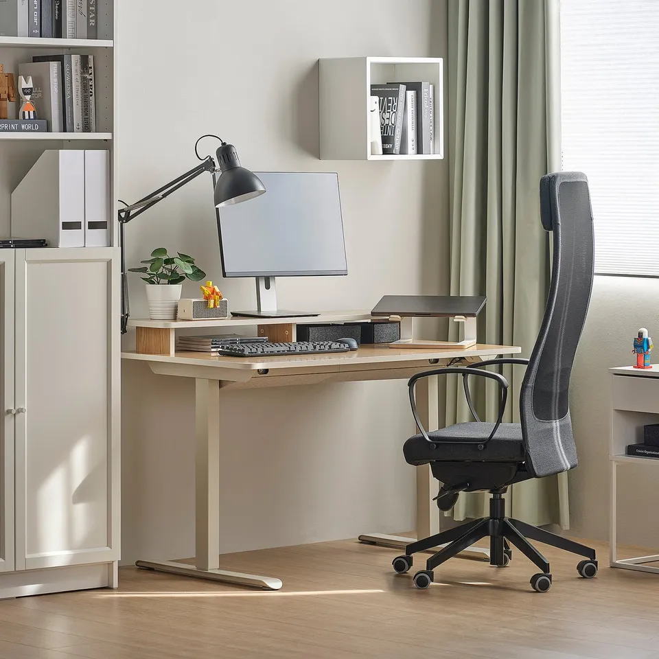 Ergonomic black office chair at wooden desk with bookshelf, monitor, and lamp.