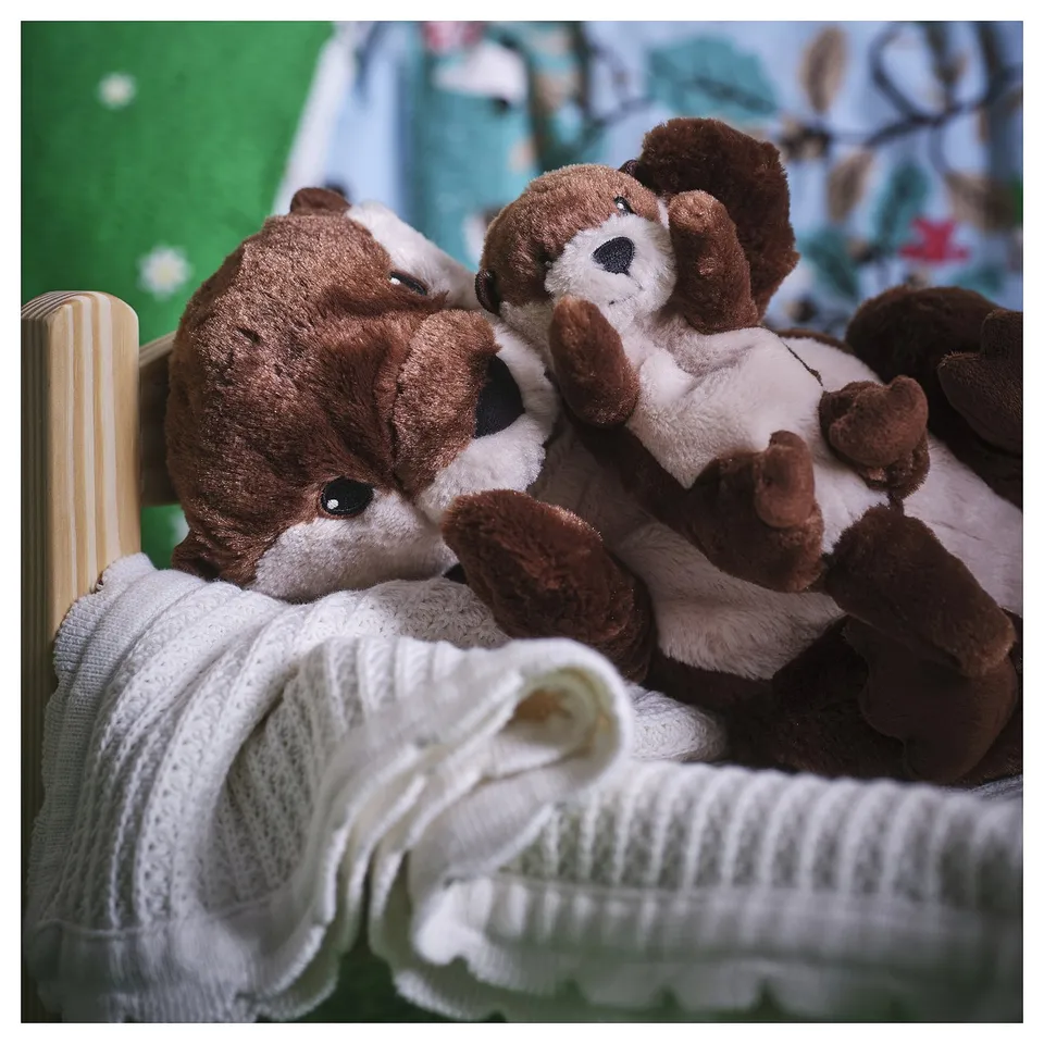 Pair of brown and white stuffed otters nestled together under white blanket on green surface.