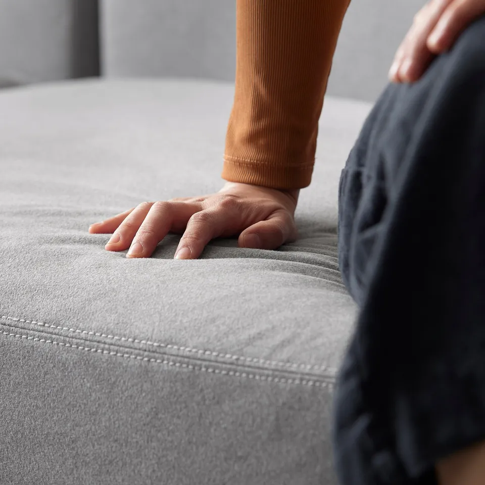 Hand touching grey JÄTTEBO sofa, modern, clean lines, comfortable.