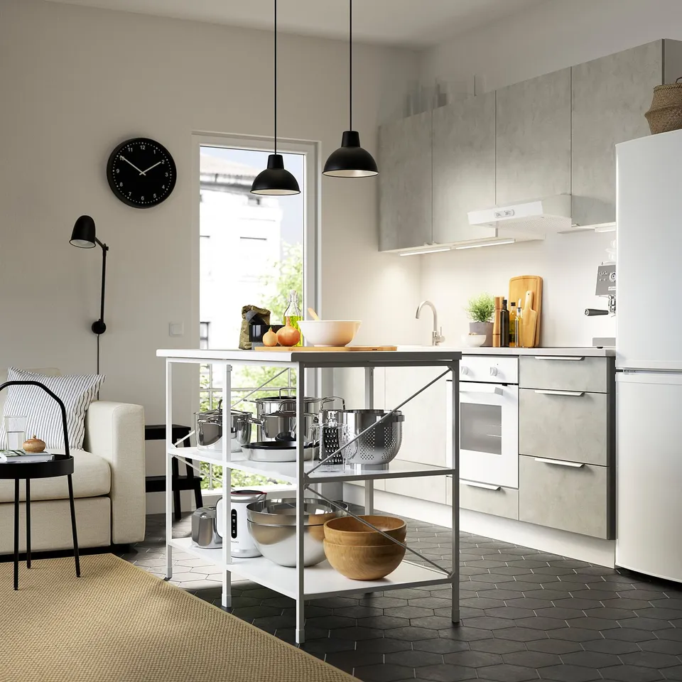 Modern kitchen with white fridge, grey cabinets, hanging lamps, and countertop island storing pots and pans.
