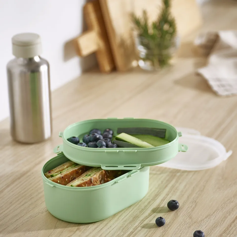 Green UTBJUDA lunch box with sandwiches and blueberries. Two tiers, polypropylene plastic. Bottle and lid nearby.