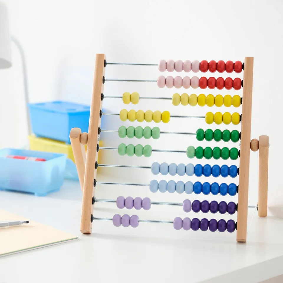 UNDERHÅLLA abacus, colourful wooden beads, light wood frame, rectangular base, folds flat, sits on a desk with notebook and pens.