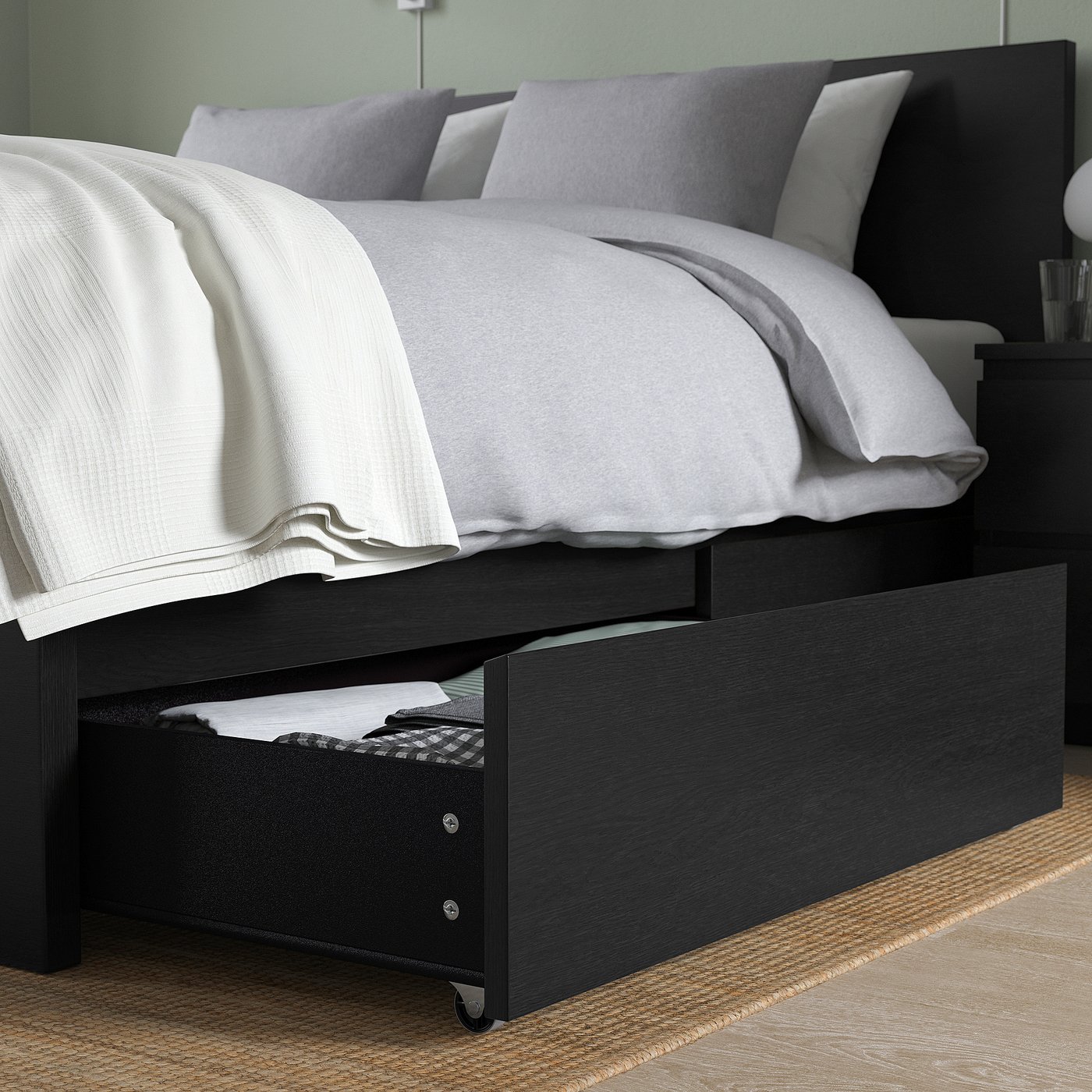 Black bed frame with drawers under for storage. White bedding on top.
