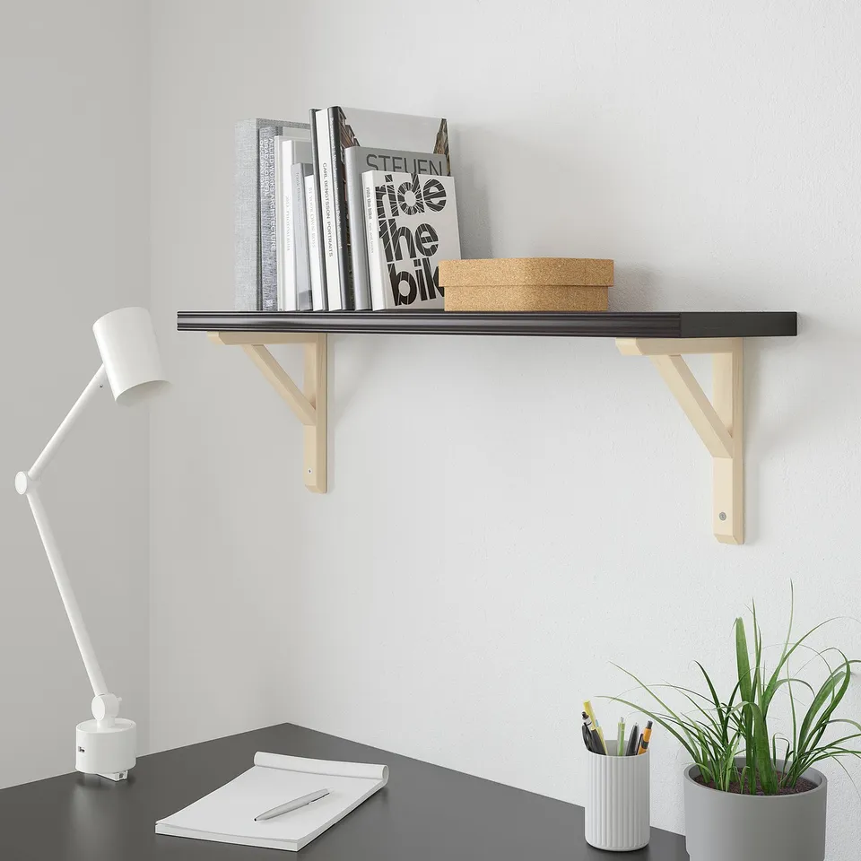 Modern black shelf BERGSHULT with wooden brackets holding books. Above desk with lamp and plant.