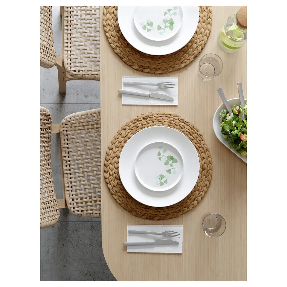 Two woven chairs beside a table set with plates, utensils, glasses, and a salad bowl.