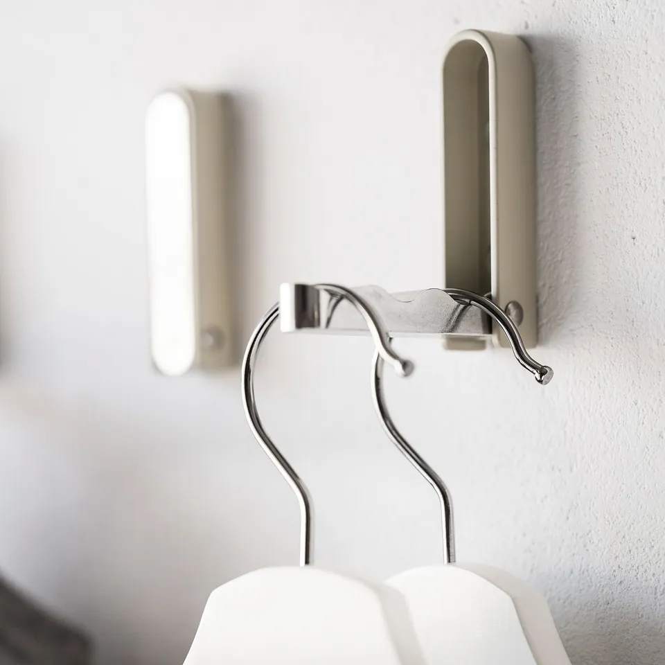 A silver KLYKET hook mounted on a white wall, holding a white hanger.