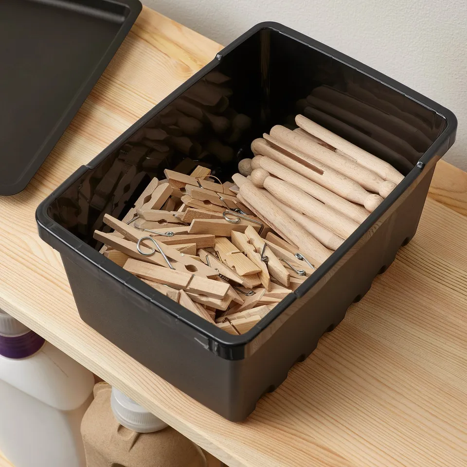 Black plastic container, holding wooden clothespins and small items, placed on a wooden shelf.