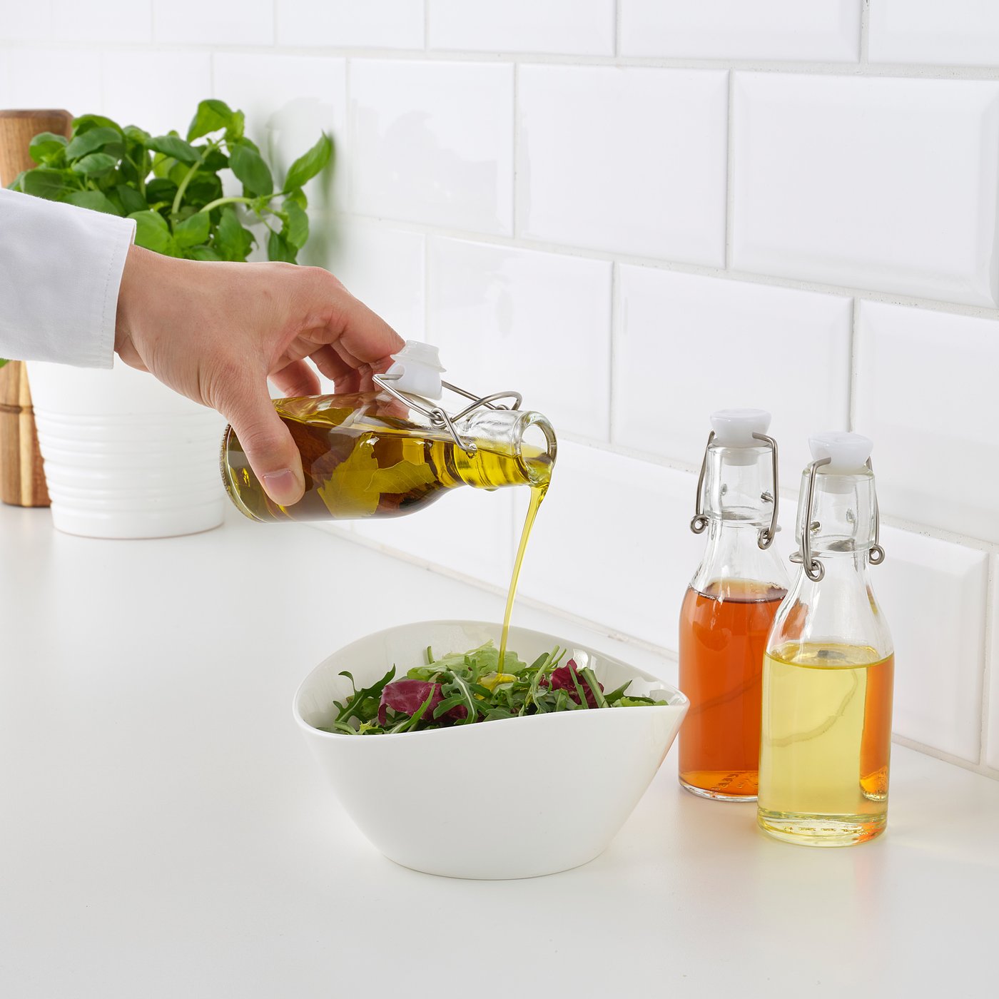 Pouring oil on salad from glass bottle. Two additional bottles beside.