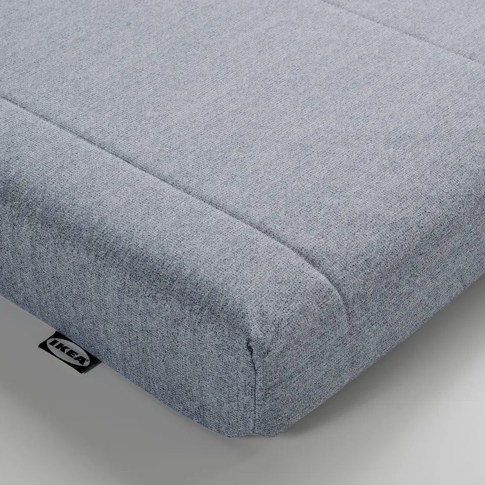 Close-up of a firm, well-stitched, light grey mattress on a white background. Tag shows ikea logo.