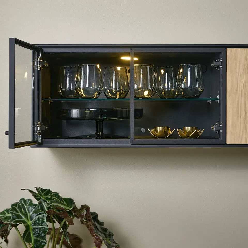 Wall-mounted glass cabinet with oak doors showcasing wine glasses and bowls. The bi-fold doors offer both storage and display functionality.
