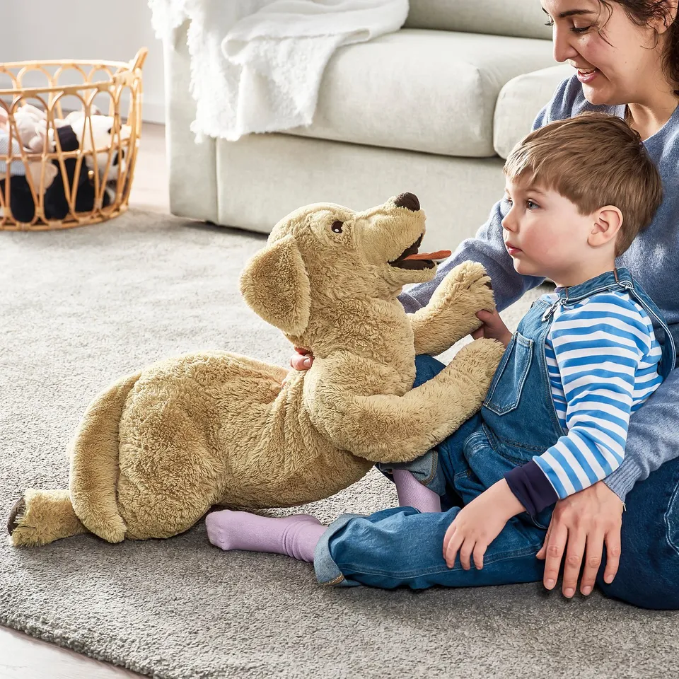 Child plays with plush golden retriever on floor, emphasising its soft, cuddly feel.
