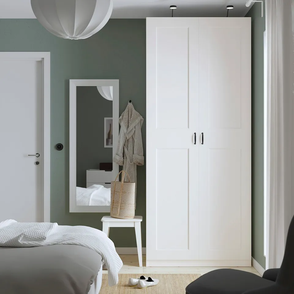 Modern bedroom with PAX wardrobe, accented mirror, stool, coat rack, and bed with white linens.