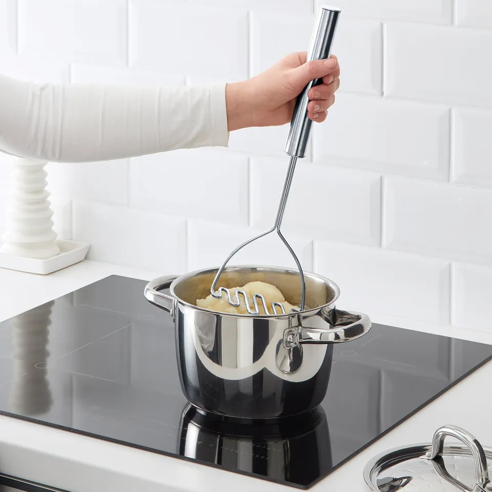 Person mashes potatoes using KONCIS potato masher with long handle on stovetop.