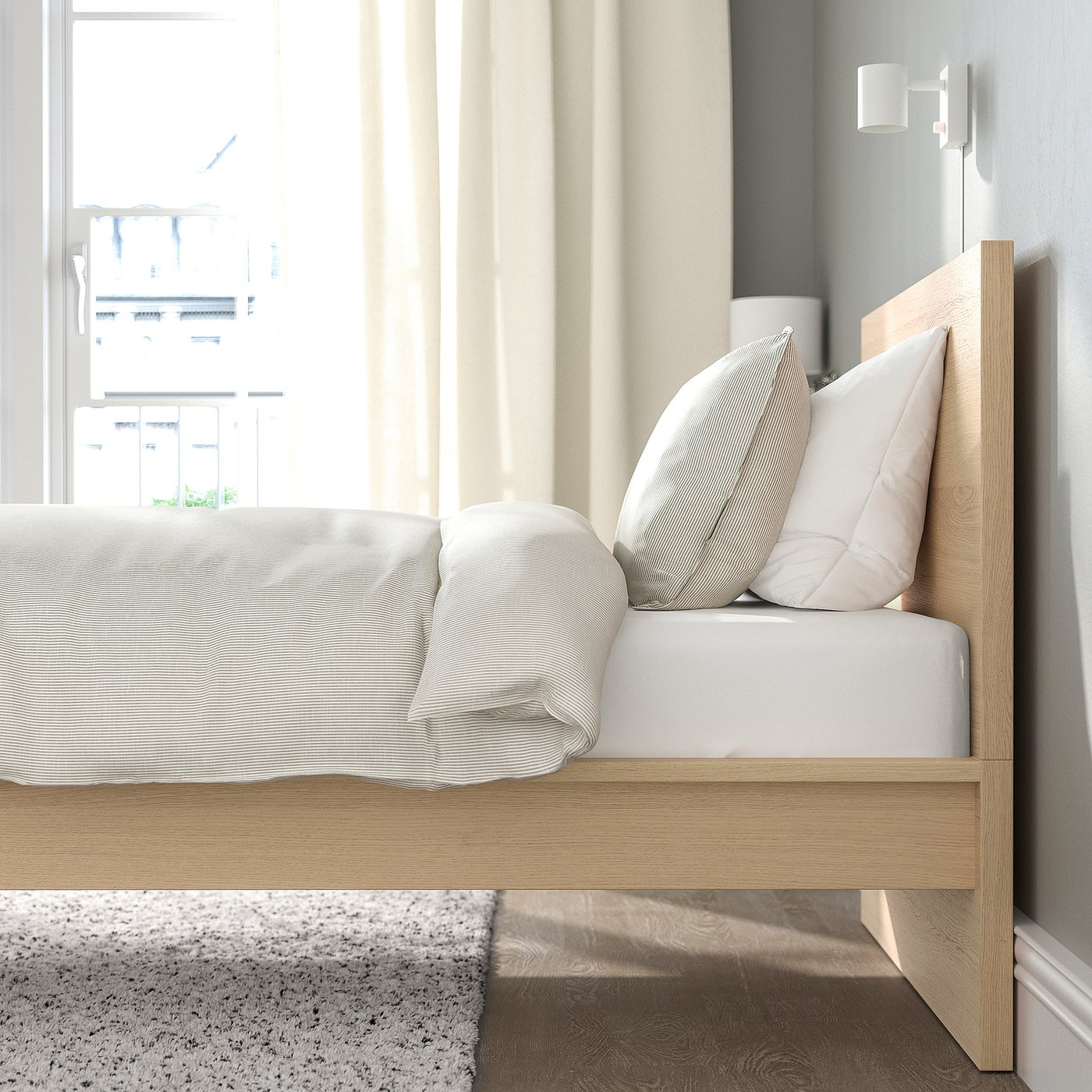 Cosy bedroom with wooden bed, white pillows, and striped blanket. Natural light fills the room.