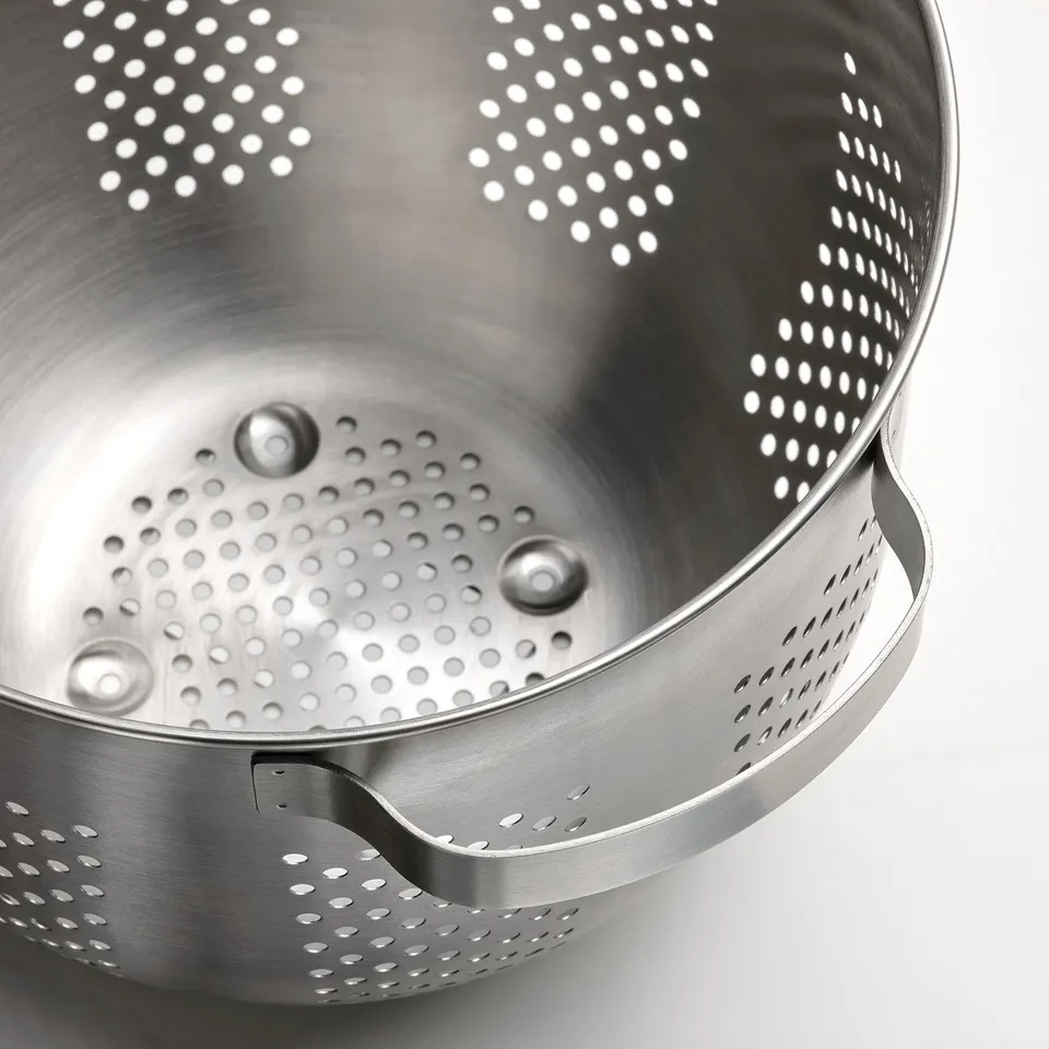 Stainless steel colander bowl with perforated holes and ergonomic handles, shown in close-up.