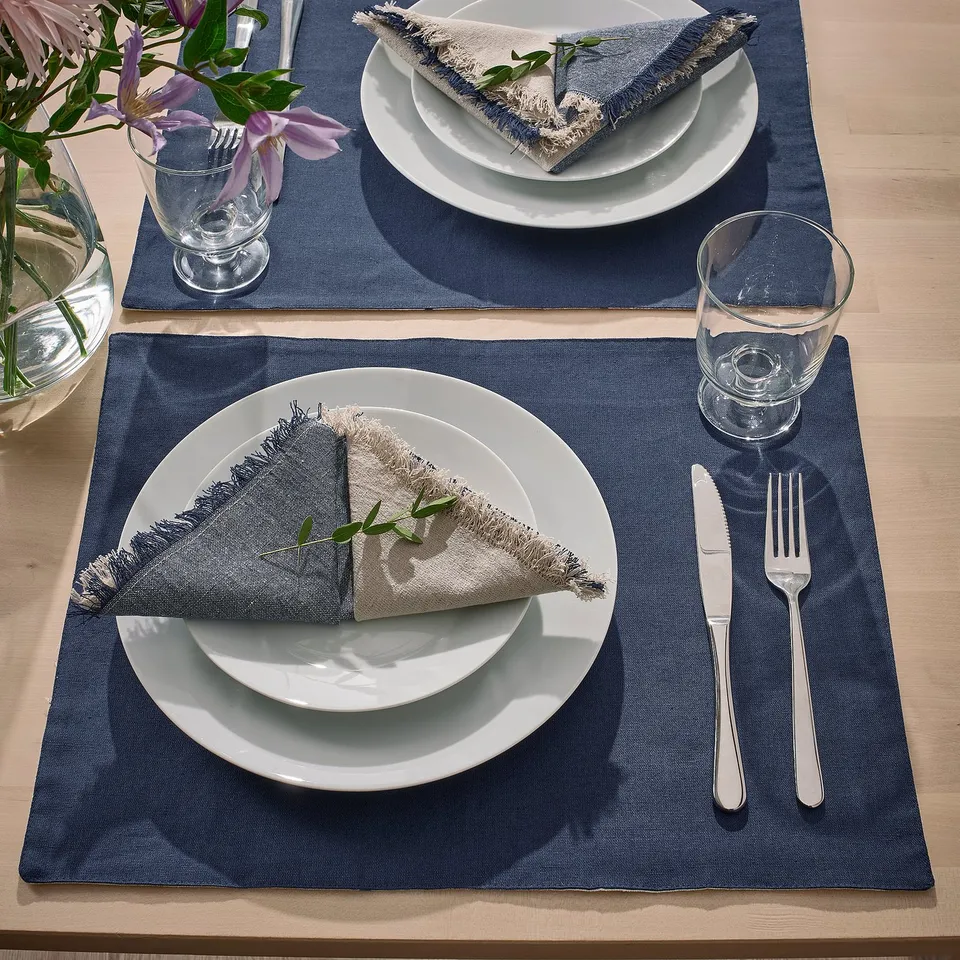 Two table settings with white plates, blue-gray napkins, clear glasses, and silverware on blue reversible place mats.