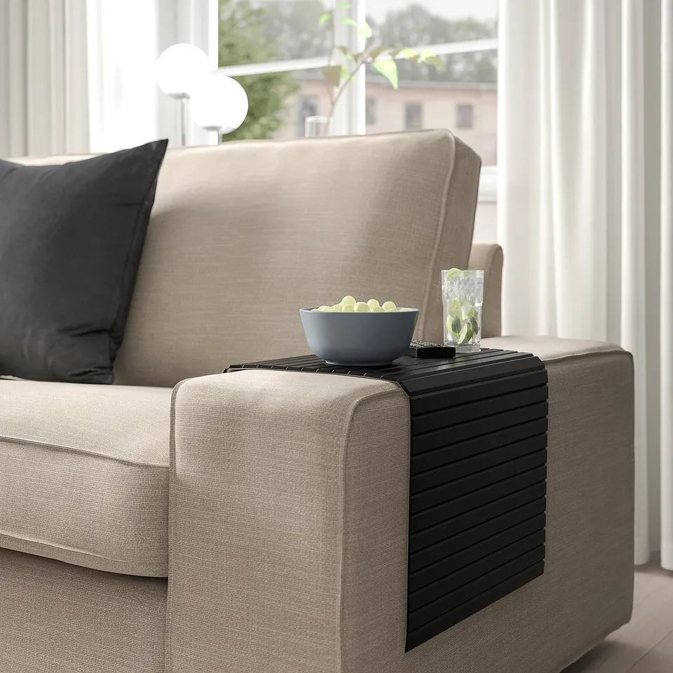 Beige sofa with black armrest tray holding bowl of fruit and drink.