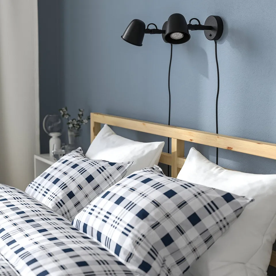 Blue plaid duvet cover on bed with wooden headboard, two black wall lamps above.
