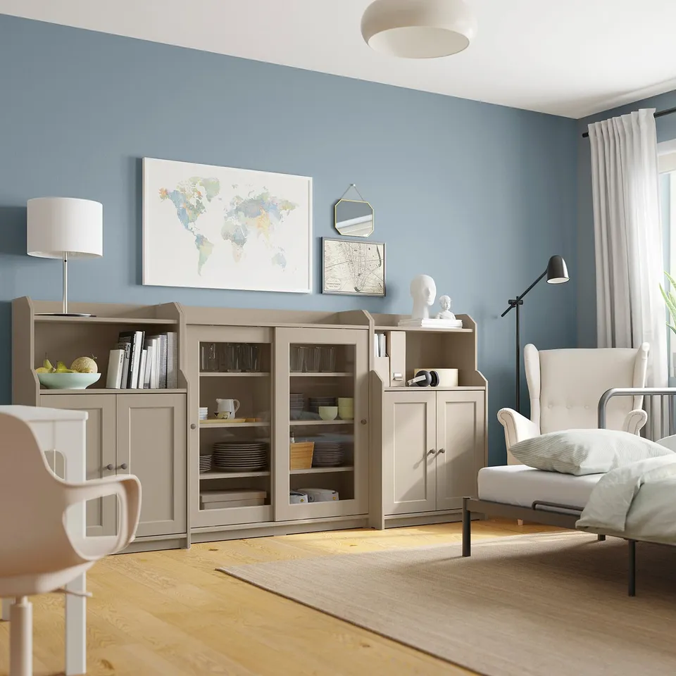 Modern living room with blue walls, featuring HAUGA storage units with glass doors, wooden floors, and white furniture including a chair and lamp.