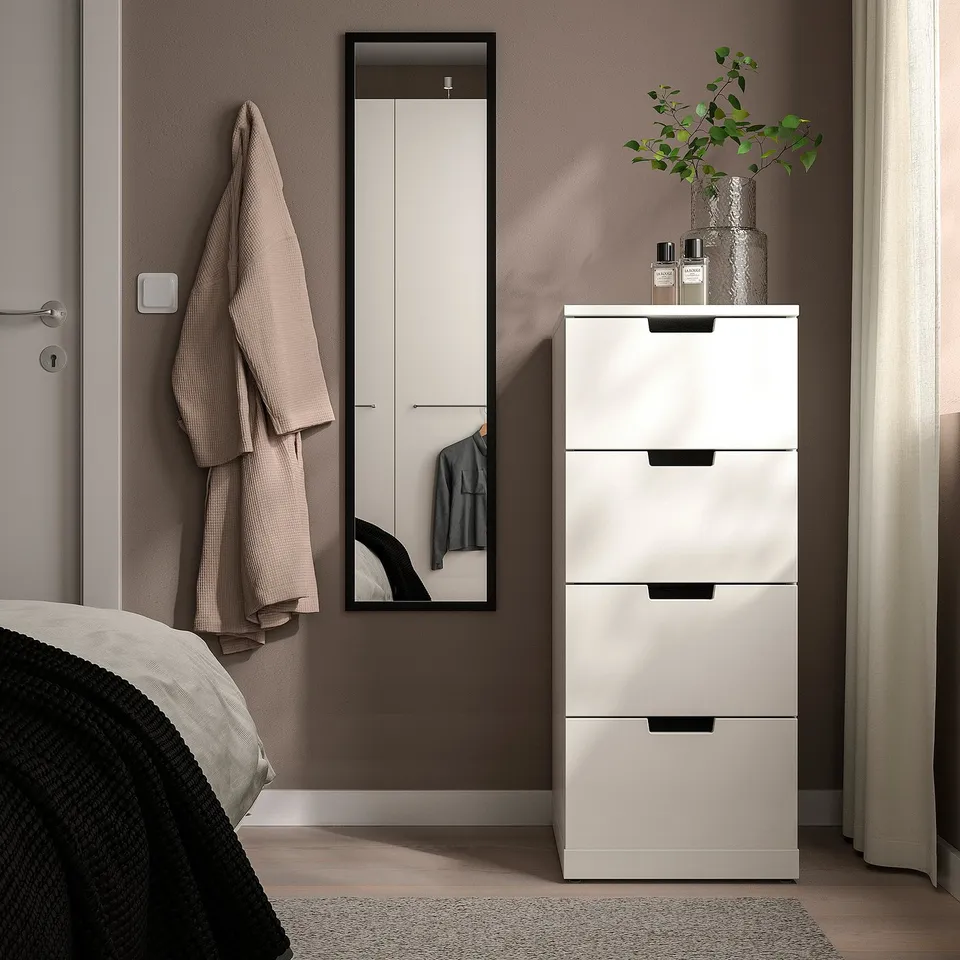 Modern bedroom with LILJETRÄD mirror, storage cabinet, towels, and vase with green leaves.