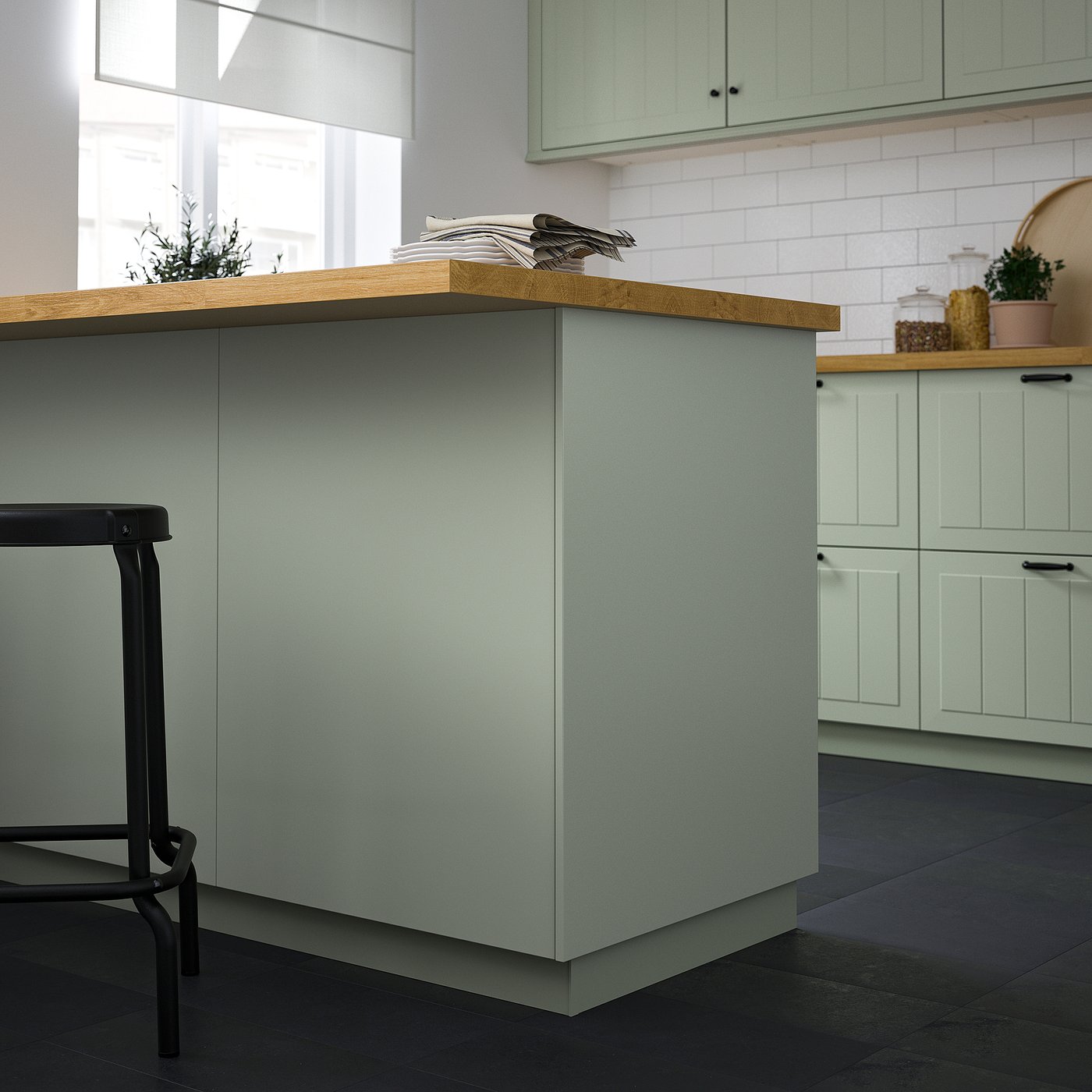 Modern kitchen with light green covers, black stools, and wood countertop.