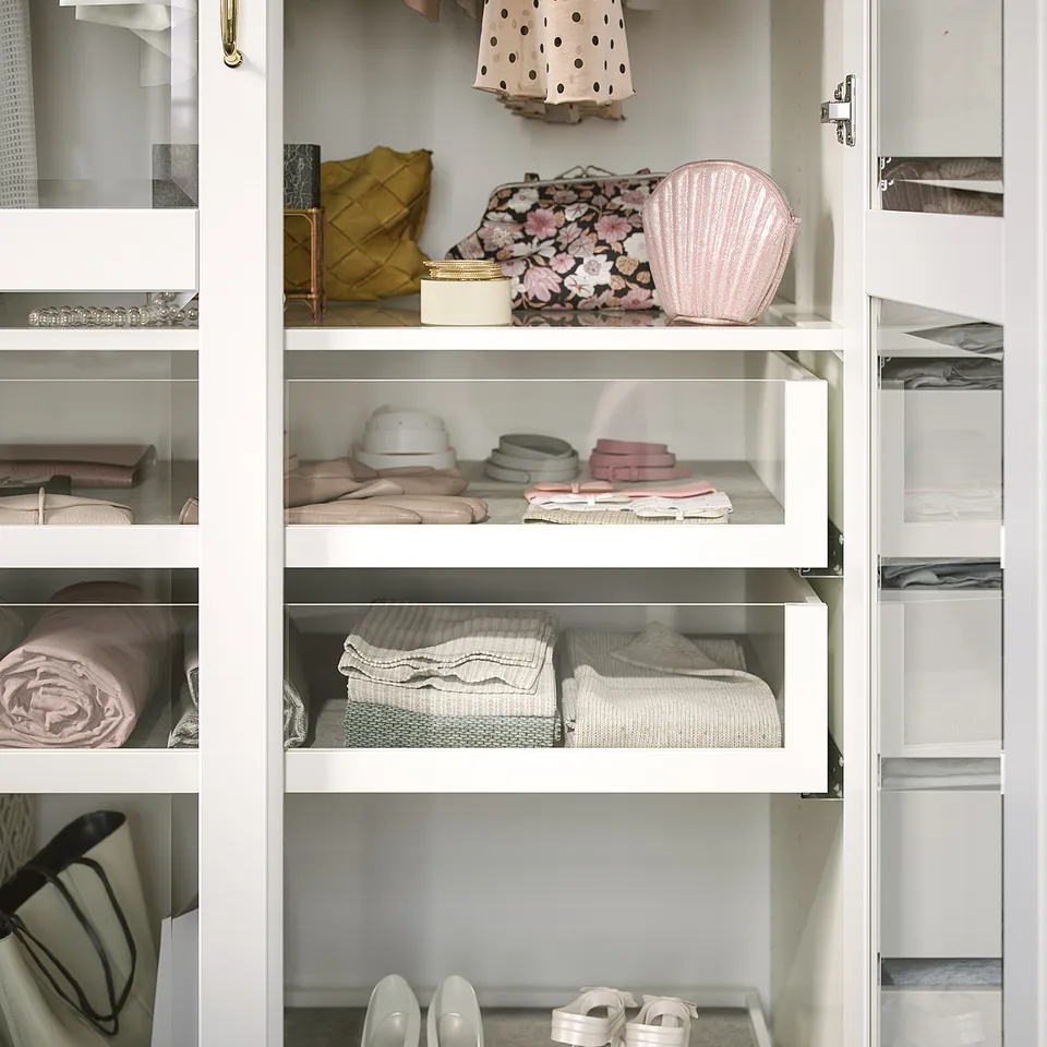 Well-organized white PAX closet with hangers, shelves, and drawers. Clothes and accessories neatly arranged in sections.
