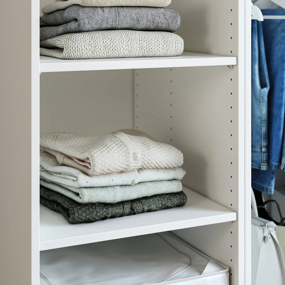 A tidy closet with folded clothes stacked on white shelves, showing organised storage.