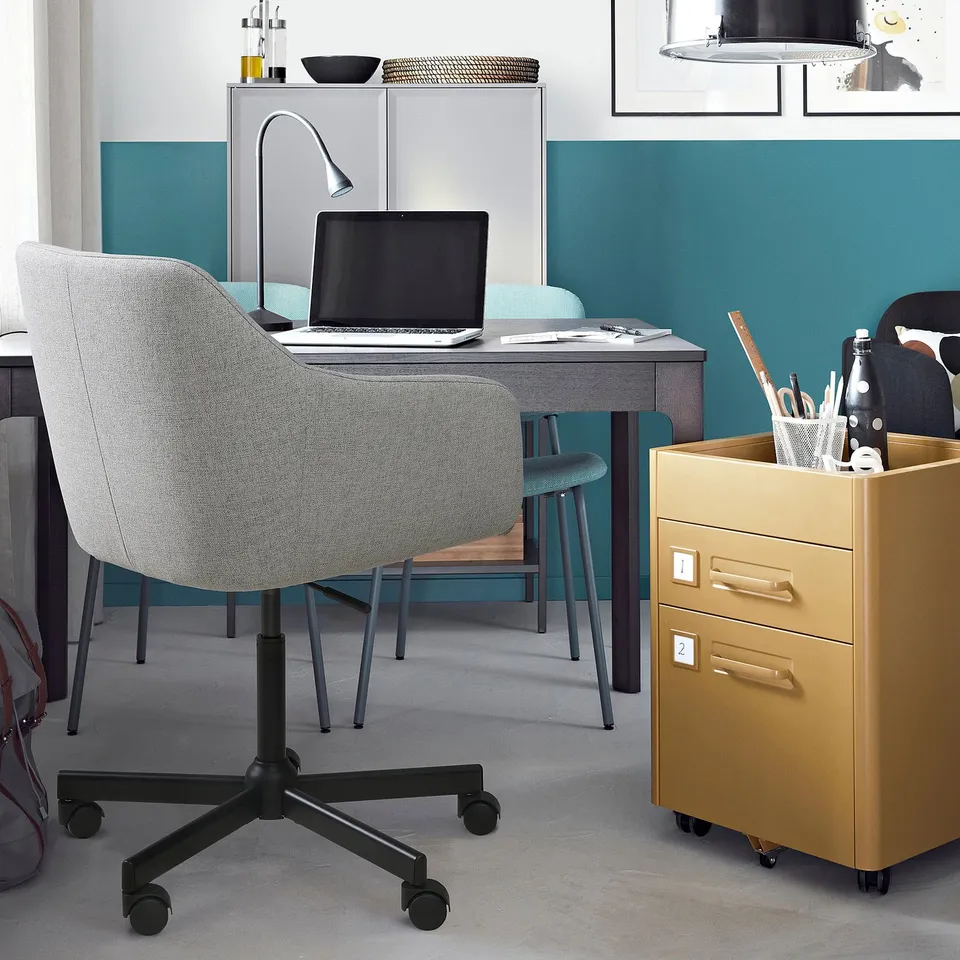 Modern home office with TOSSBERG swivel chair, wooden desk, and gold storage cabinet. Teal walls complement organised workspace.