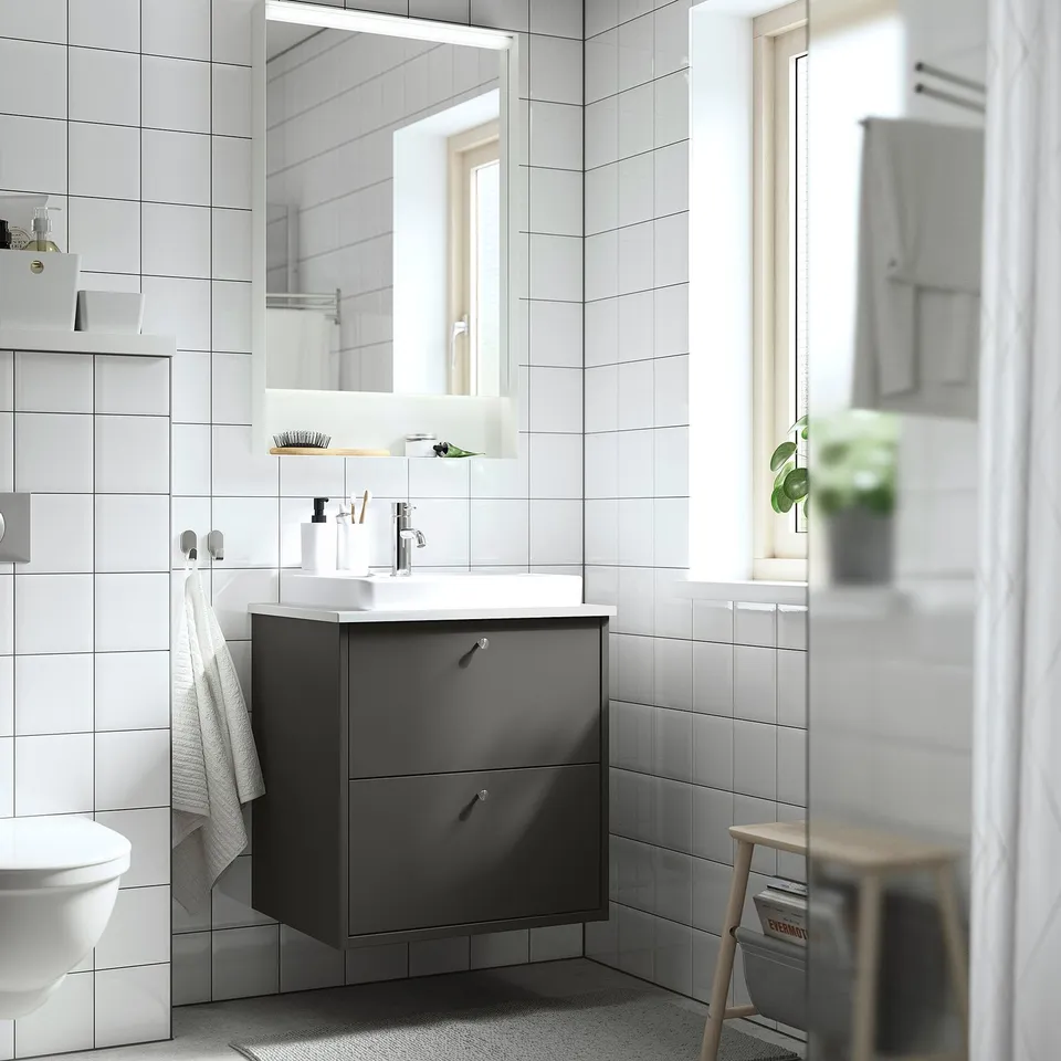HAVBÄCK dark wash-stand with 2 drawers & white basin in modern bathroom. Tiled wall, crisp surroundings, and wooden stool.