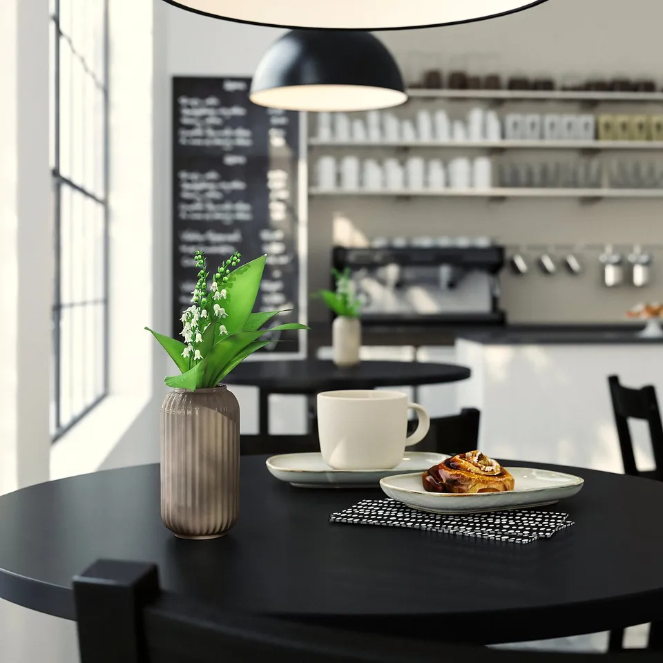 Cosy café with a black table, white cup, pastry, and dark cylindrical STILREN vase with white flowers.