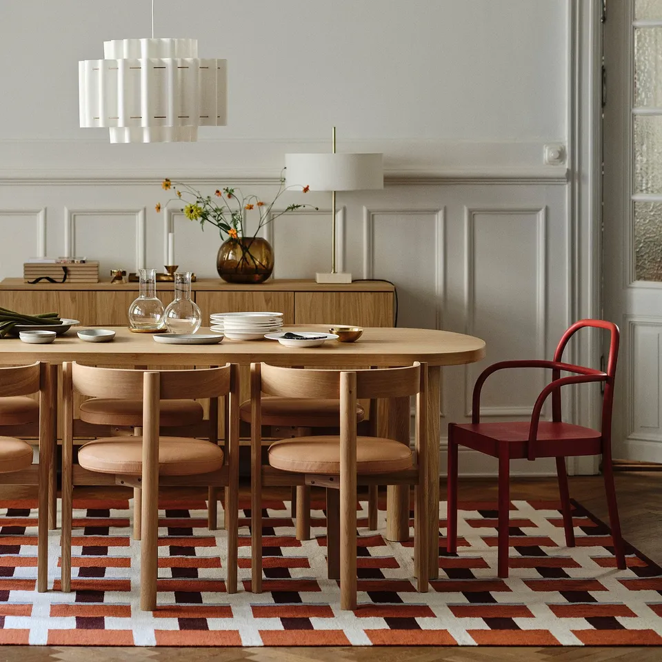 Modern dining room with oval wood table, six chairs, colourful rug, and pendant lamp.