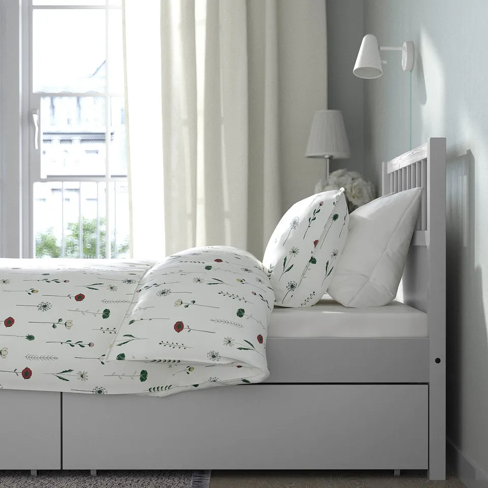 White wooden bed with floral bedding, two pillows, bedside lamp, headboard, footboard, and storage.