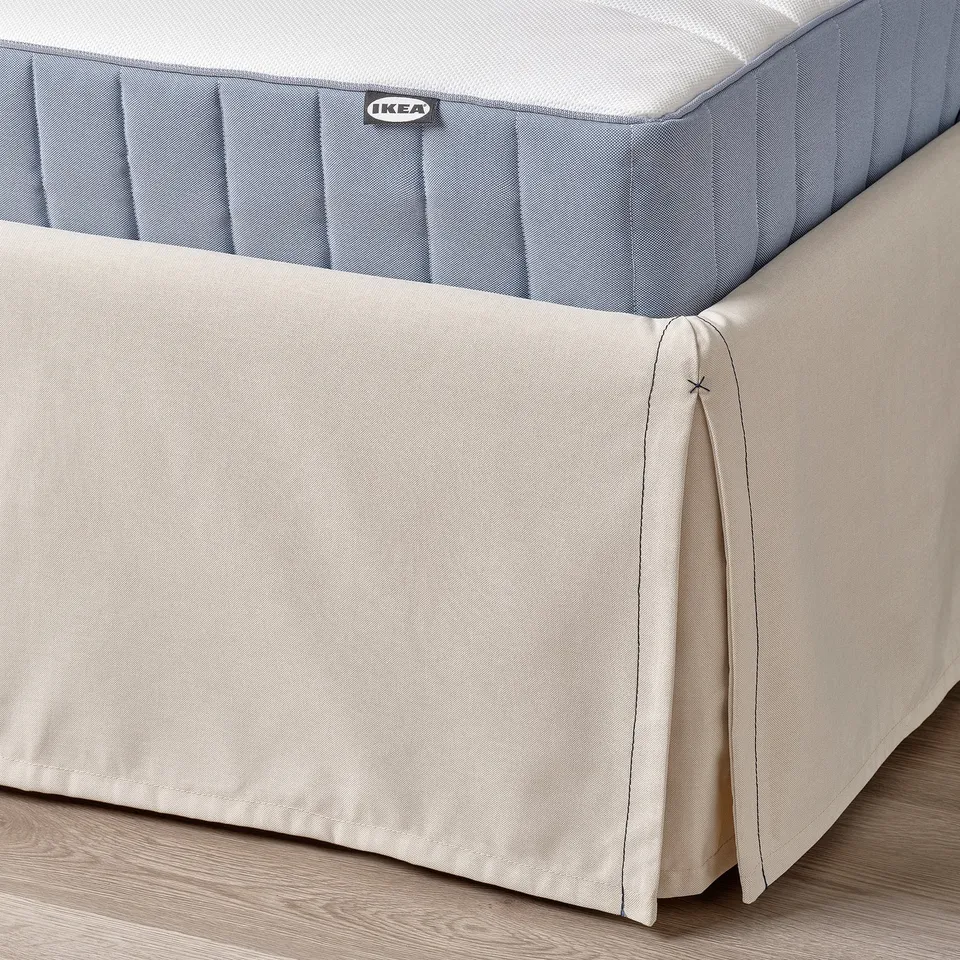 Beige bed skirt on wood floor, machine washable, decorative stitching, hides storage.