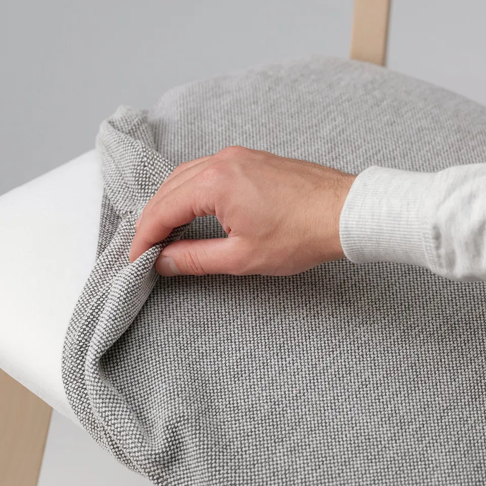 Hand adjusting removable, washable chair cover on wooden chair frame.