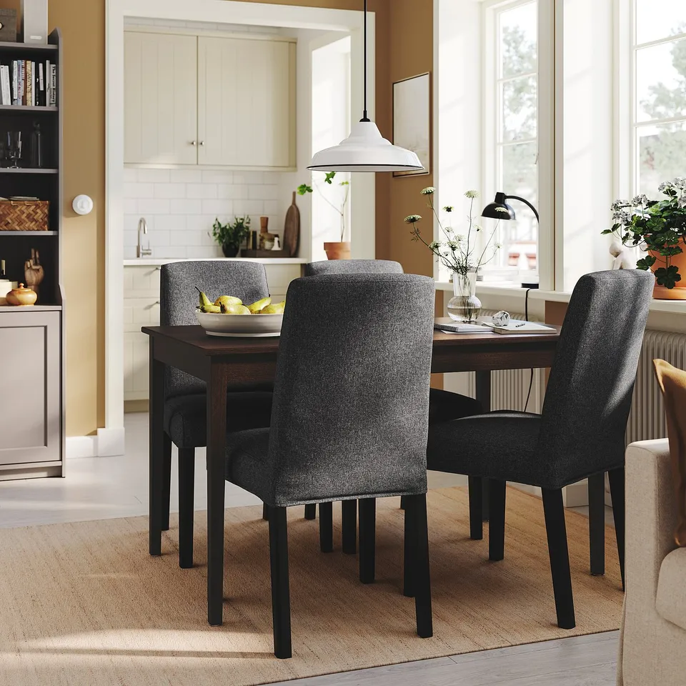Dark dining table with four grey chairs, set near a large window in a cosy kitchen.
