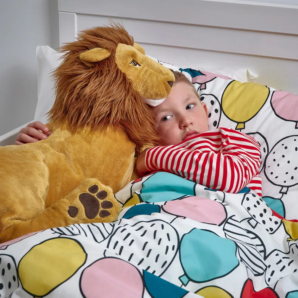 A child cuddles a large stuffed lion toy in bed.