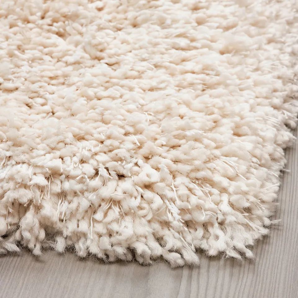 Close-up of thick, shaggy rug with soft, uneven texture. Cream-colored yarn creates inviting, comfortable feel.