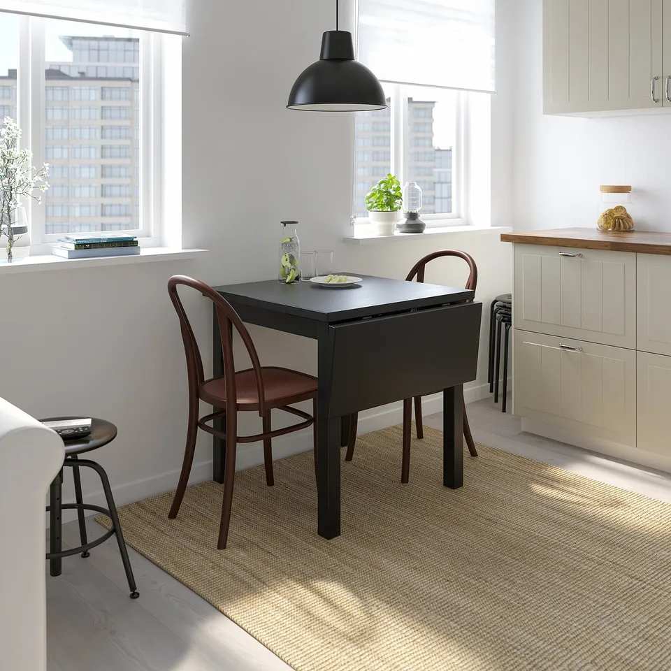 A modern kitchen with a black NORDVIKEN drop-leaf table, seating two brown chairs. The tables compact design saves space, ideal for small areas.