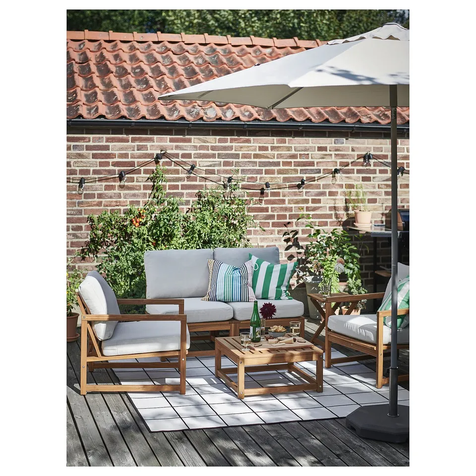 Patio with wooden furniture, cushions, striped pillows, table, bottle, umbrella, lights, brick, and tile roof.