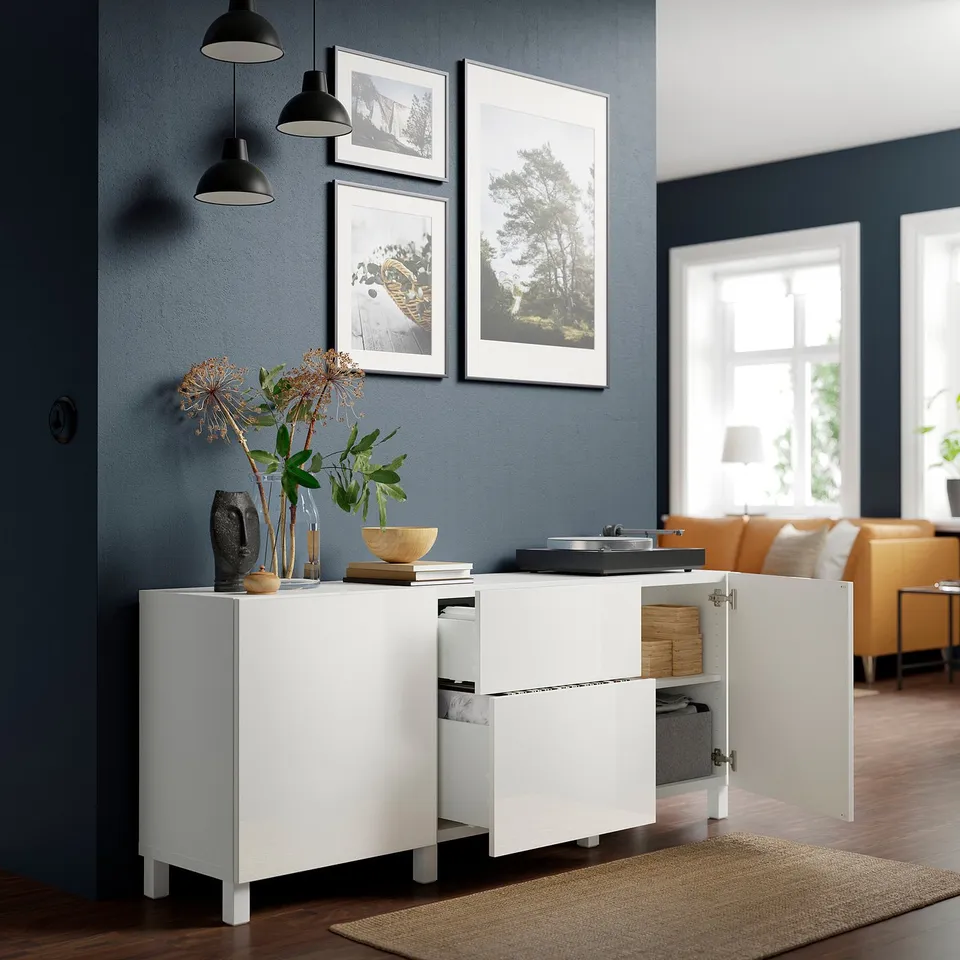 Modern white cabinet with open storage, glossy front, dark blue wall, pendant lights, and decor.