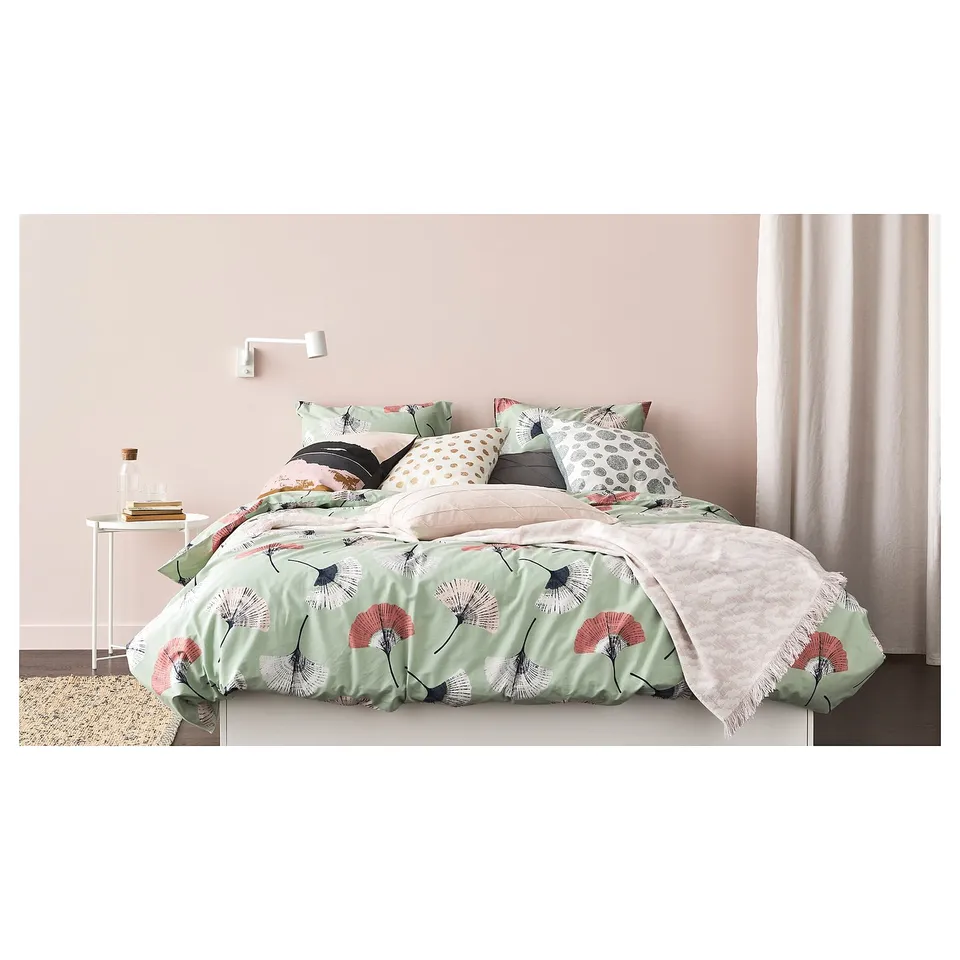 Bed with floral print blanket, pink accents, and pillows. Bedside table with books and glass jar.