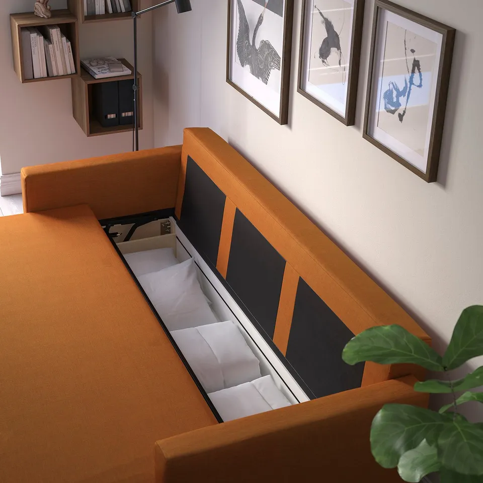 Orange convertible sofa with storage open, showing bedding and pillows, against wall with art.