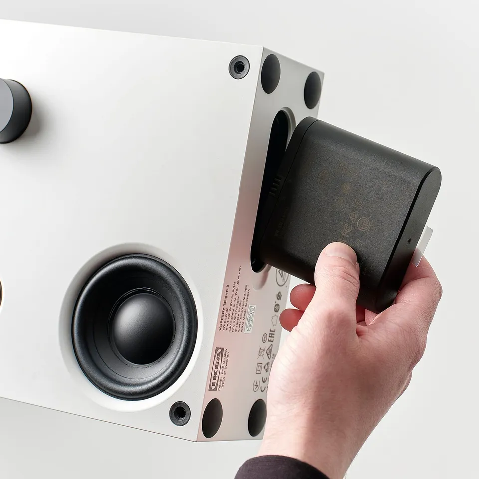Hand presses button on black VAPPEBY bluetooth speaker against white speaker, controlling playback.
